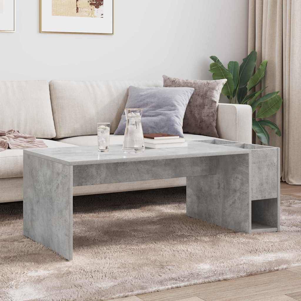 Ein modernes Wohnzimmer mit einem beigen Sofa, verschiedenen Kissen und einem grauen Betoncouchtisch auf einem hellen Teppich. Zwei gerahmte Bilder und eine Pflanze dienen als Dekoration.
