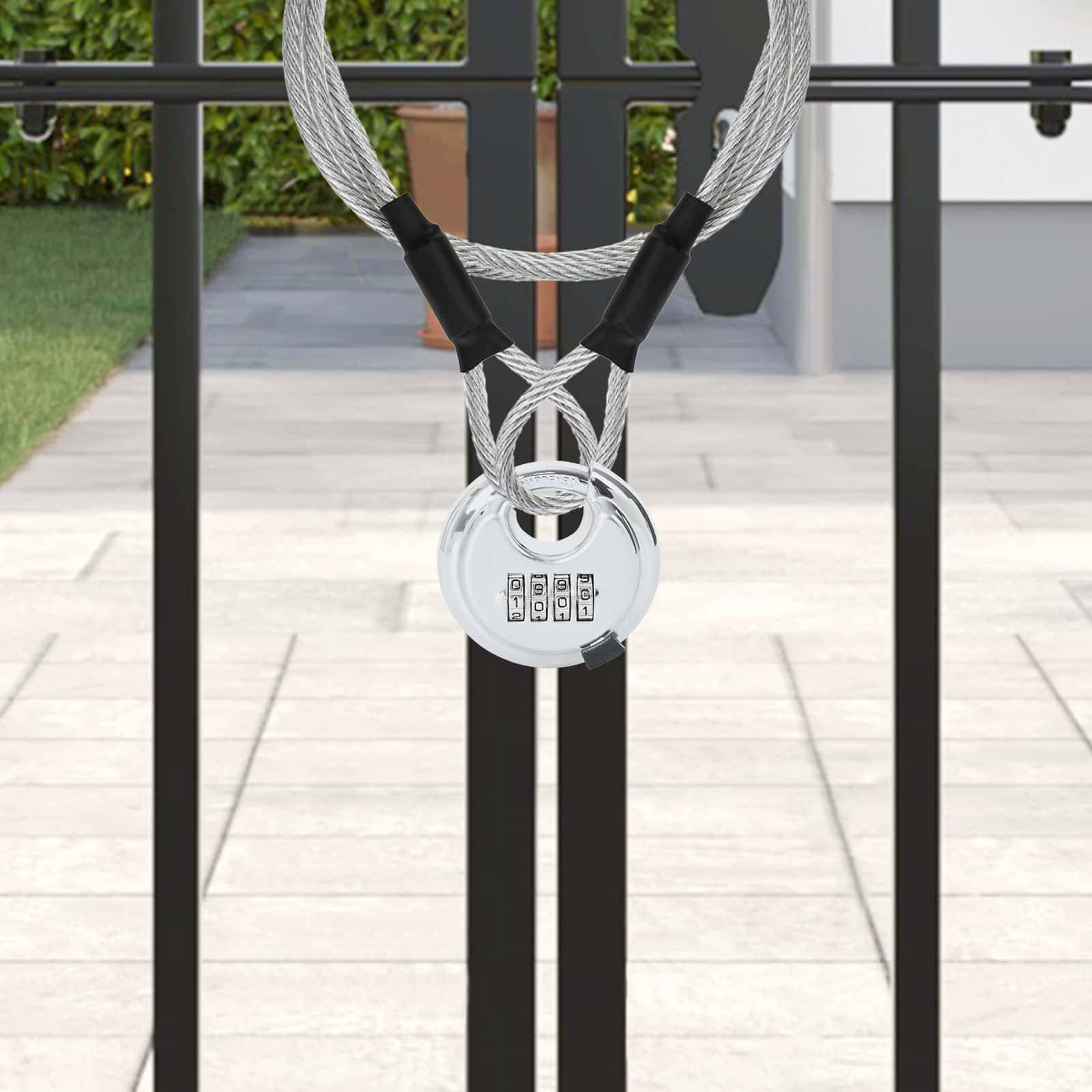 Ein schwarzes Metalltor ist mit einem Zahlenschloss und einem Kabel gesichert. Im Hintergrund sind ein Garten mit grünen Sträuchern und ein Topf sichtbar.