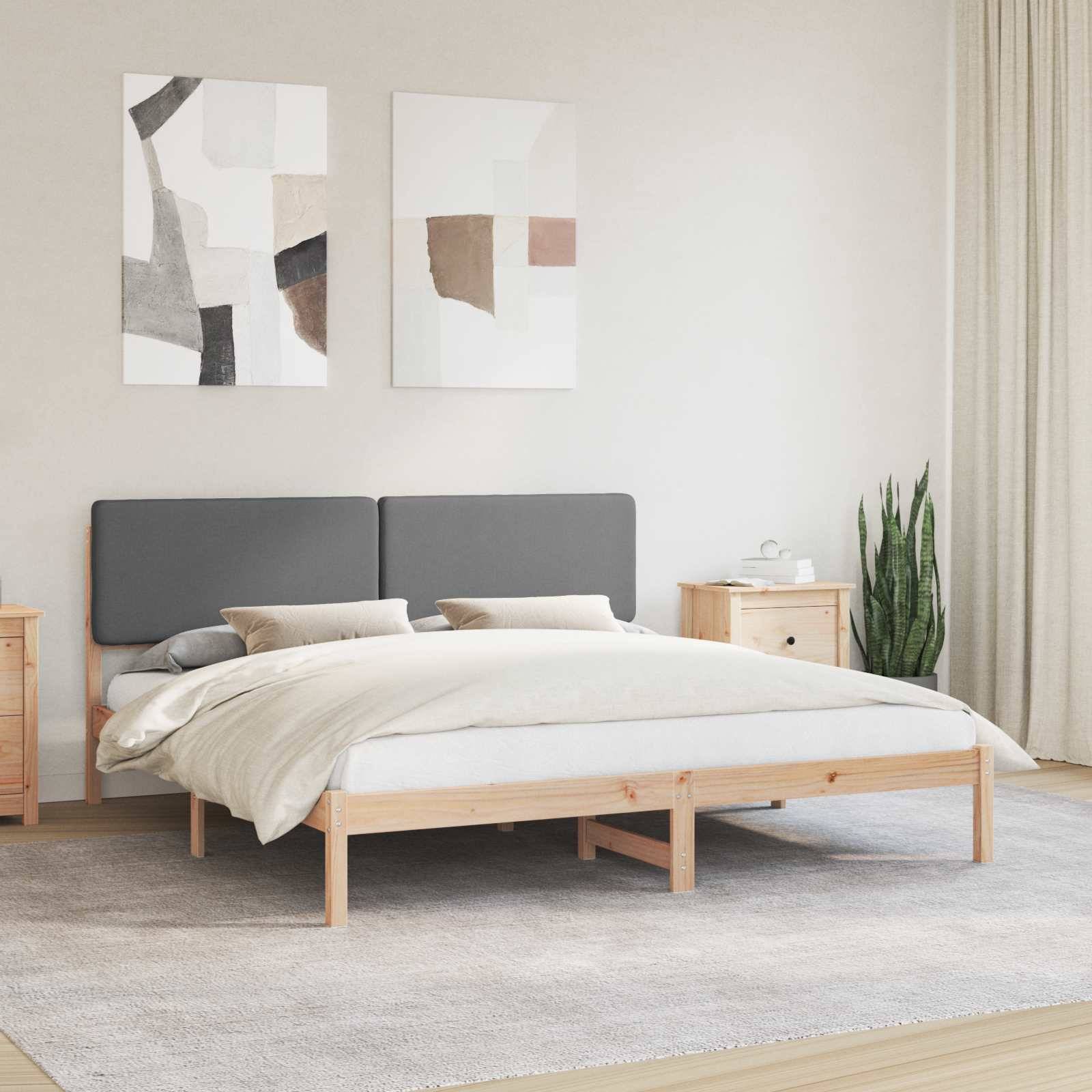 Ein ordentlich eingerichtetes Schlafzimmer mit einem Holzbett, grauem Kopfteil, zwei Kissen und einer weißen Steppdecke. Zwei abstrakte Kunstwerke hängen über dem Bett.
