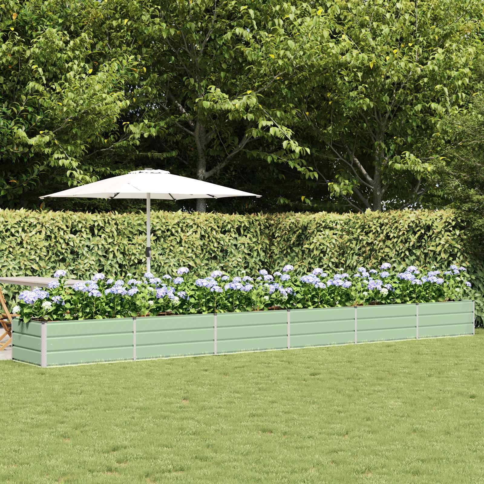Ein langes, hellgrünes erhöhtes Hochbeet mit blauen Hortensien steht auf einem Rasen, dahinter eine Hecke und Bäume, mit einem weißen Schirm in der Nähe.