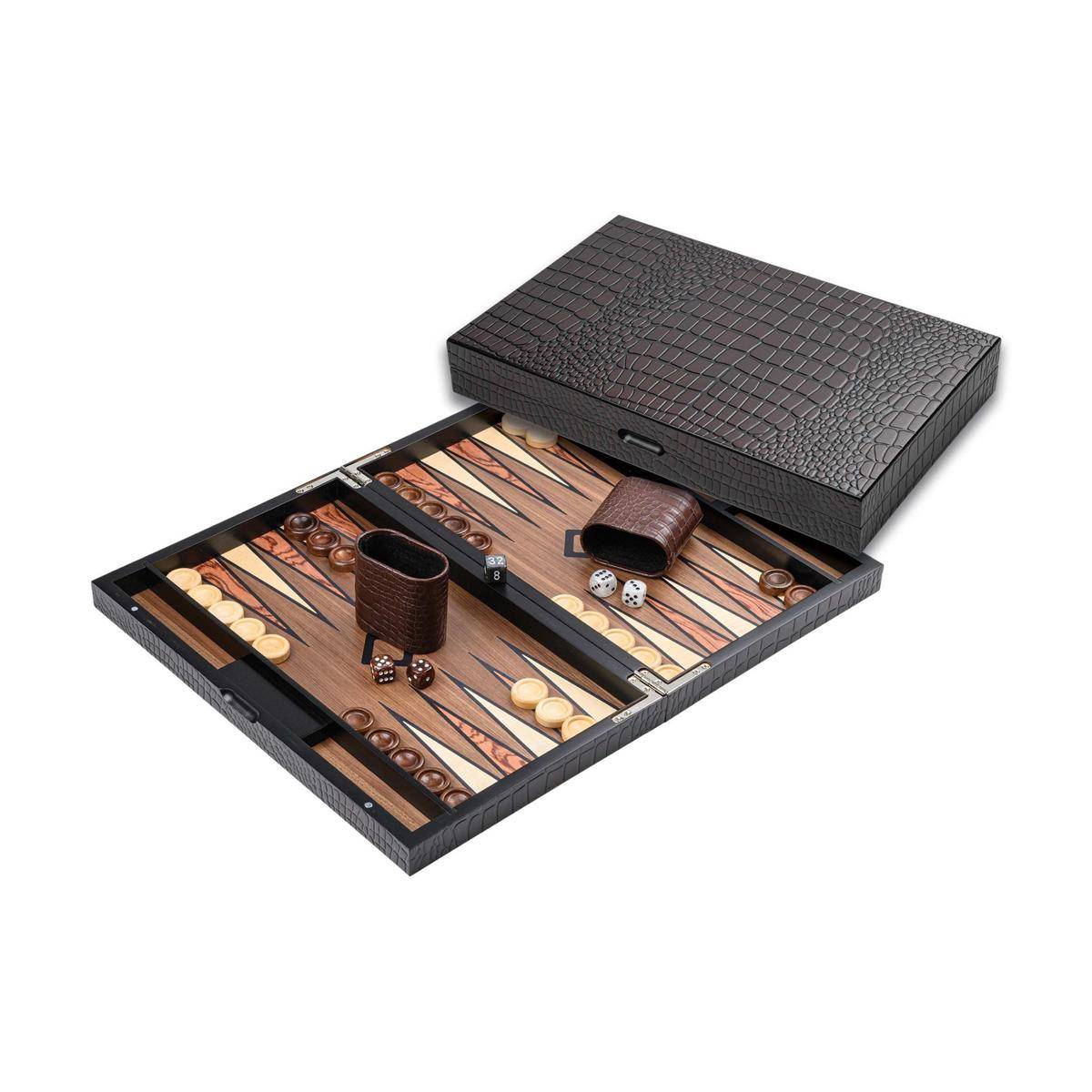Ein Backgammon-Brett mit Steinen, Würfeln und Würfelbechern auf einem offenen Koffer mit Krokodilmuster auf der Außenseite.