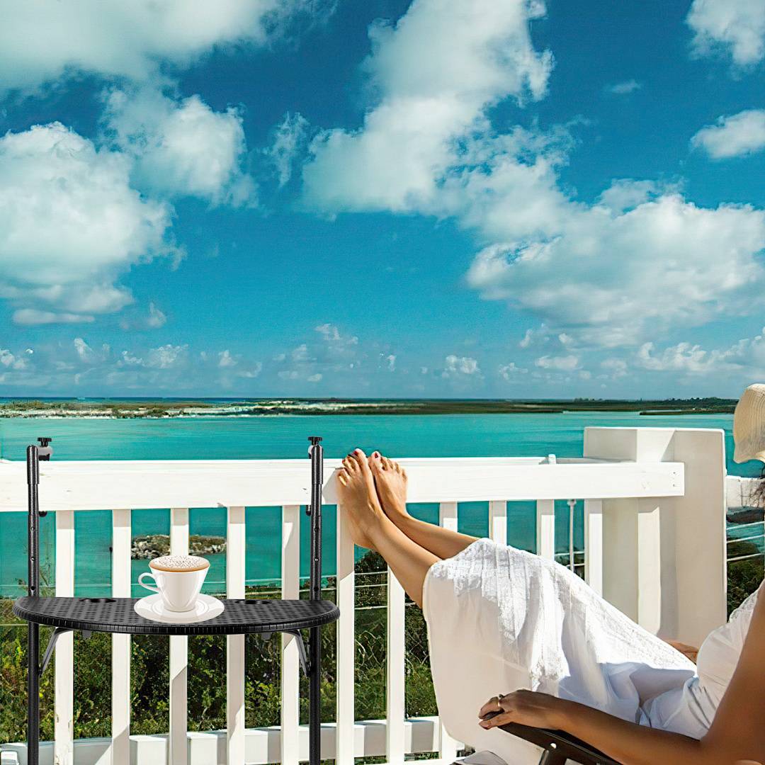 Eine Person entspannt sich mit einem Getränk auf einem Balkon mit Blick auf einen ruhigen türkisblauen Ozean unter einem blauen Himmel mit flauschigen Wolken.