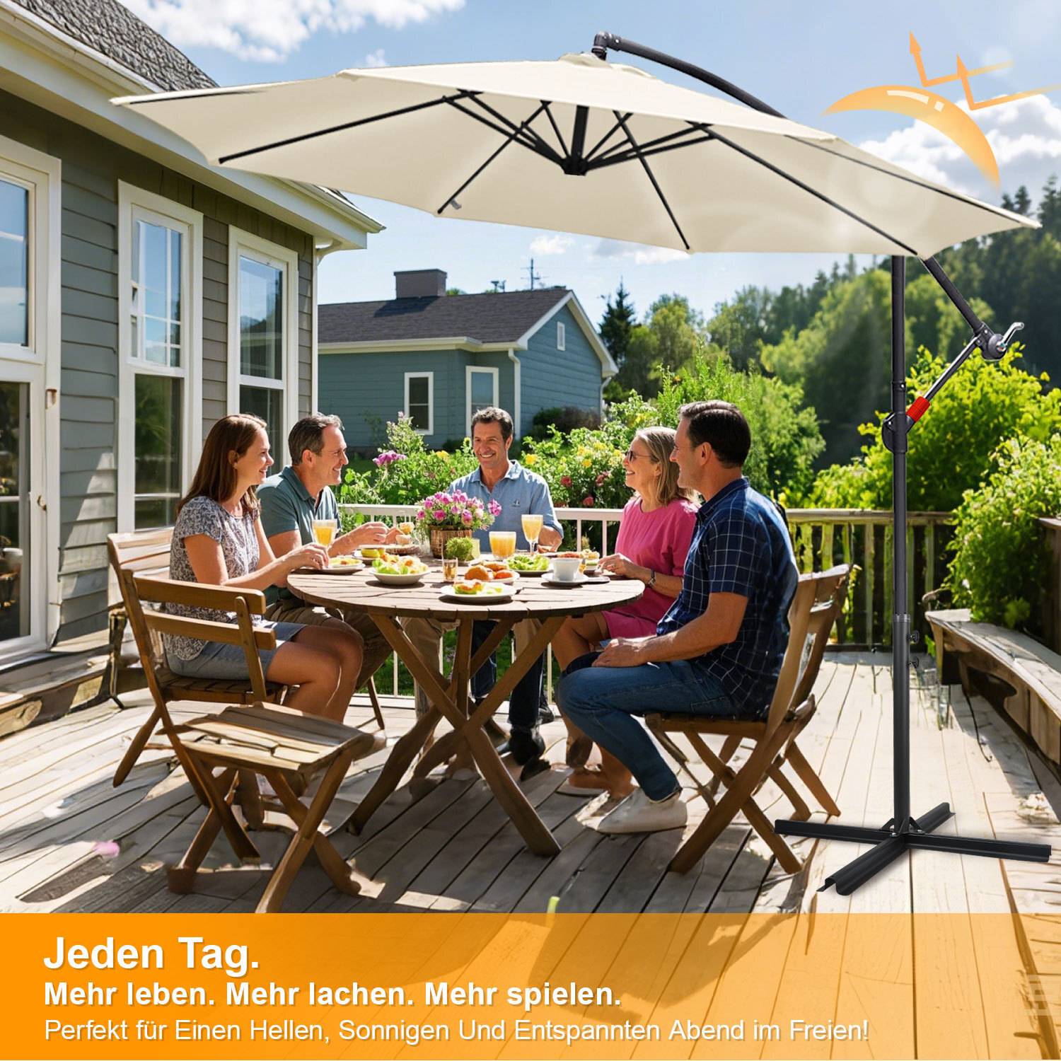 Eine Gruppe von Personen sitzt um einen Tisch im Freien und genießt eine Mahlzeit unter einem großen Regenschirm. Im Hintergrund sind Bäume und ein Haus zu sehen.