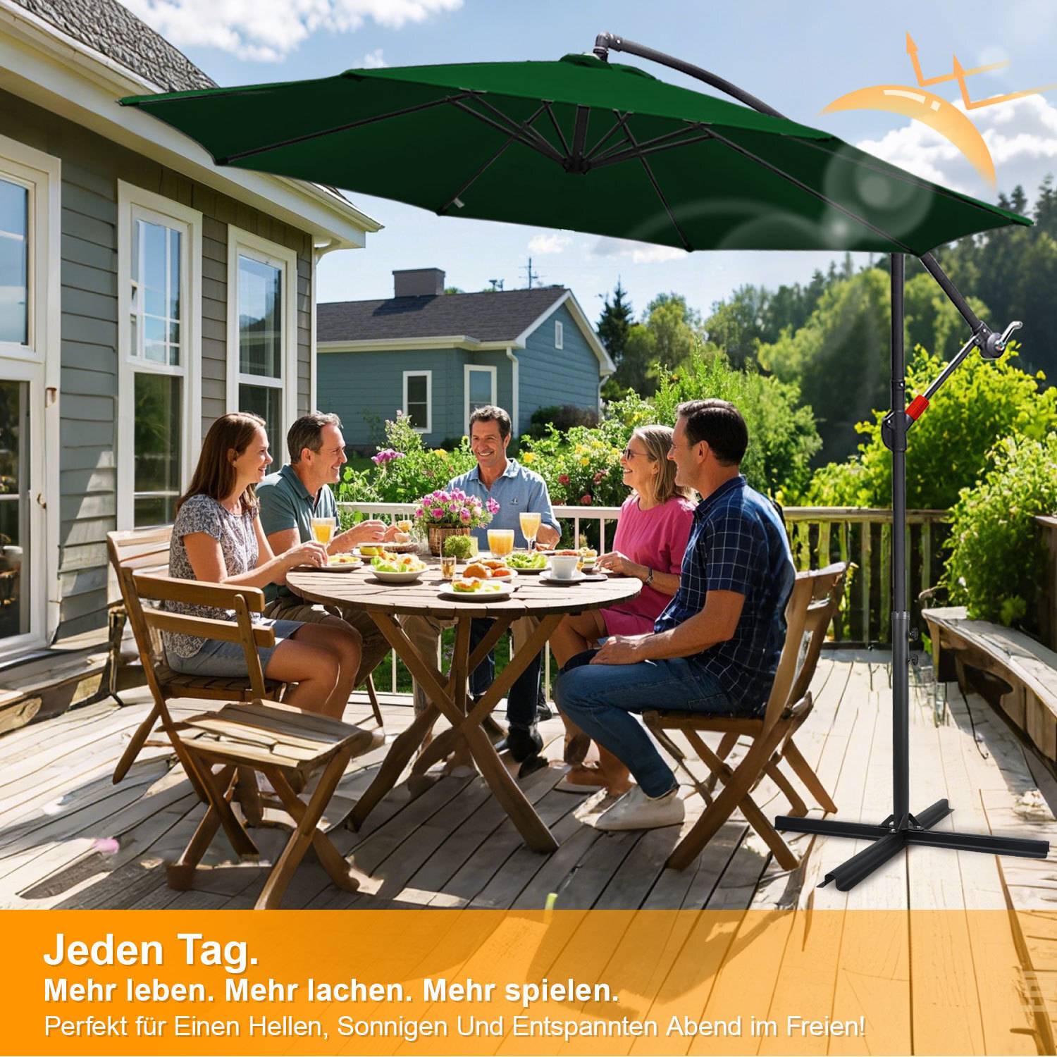 Eine Gruppe von Menschen, die um einen Tisch herum sitzen und auf einer sonnigen Holzterrasse mit einem offenen Regenschirm eine Mahlzeit genießen. Gärten und Bäume im Hintergrund.