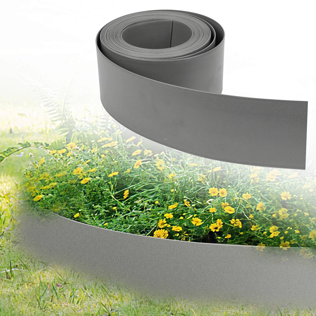 Eine Rolle flexible graue Gartenumrandung ist zu sehen, teilweise um ein Blumenbeet mit gelben Blumen auf einem Rasen entrollt.