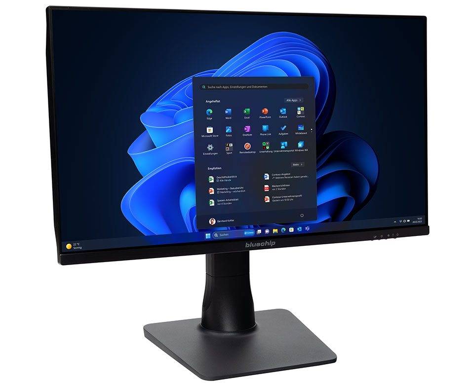 Ein Computermonitor zeigt das Windows 11-Startmenü mit verschiedenen Anwendungssymbolen vor einem blauen abstrakten Hintergrund an.