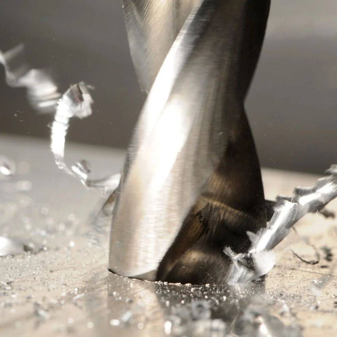 Eine Nahaufnahme eines rotierenden Bohrers, der in eine Metalloberfläche eindringt, mit verstreuten Metallspänen rundherum, die industrielle Bearbeitung illustrierend.