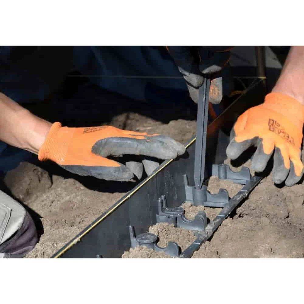 Zwei Personen tragen orange Handschuhe und installieren eine schwarze Kunststoff-Landschaftseinfassung in den Boden, wobei sie Pflöcke zur Sicherung verwenden.