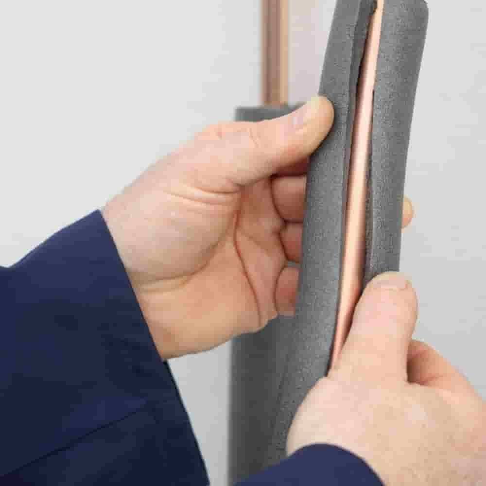 Eine Person, die ein Stück Schaumrohr-Isolierung um ein Kupferrohr hält, demonstriert, wie man Rohre zur Energieeffizienz isoliert.