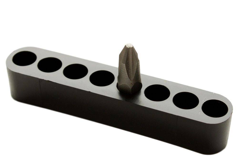 Ein einzelner Senkerbohrer wird in eine Reihe von leeren runden Löchern in einem dunkelgrauen Block eingesetzt. Der Bohrer ist metallisch und läuft spitz zu.