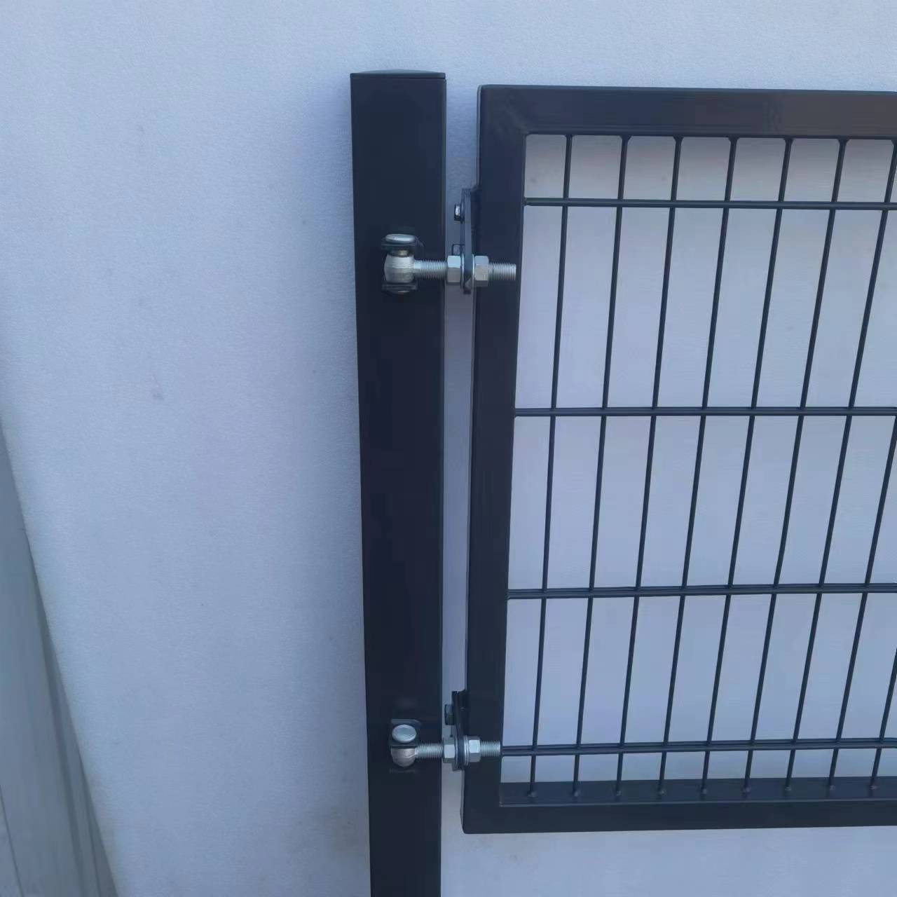 Metallisches Torriegel-Schließmechanismus an einer weißen Wand angebracht, zeigt der Schließmechanismus und die Scharnier-Details.