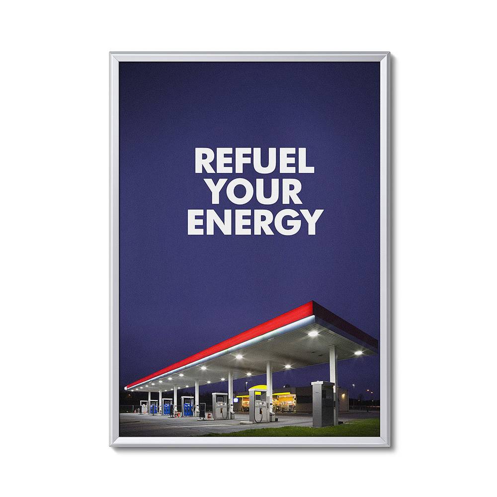 Ein gerahmtes Fotografie einer Tankstelle mit einem roten Vordach in der Abenddämmerung, mit dem Text „Tanken Sie Ihre Energie auf