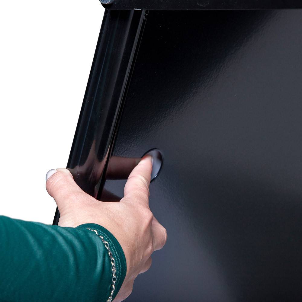 Eine Hand, die einen schwarzen Müllsackspender an der Wand öffnet.