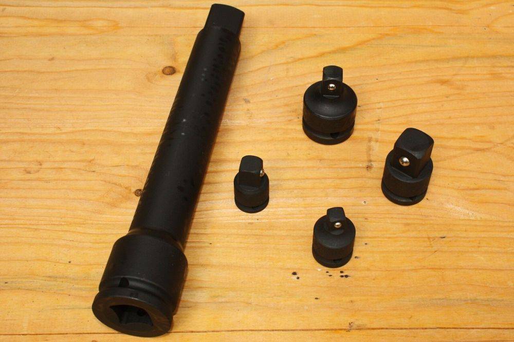 Ein schwarzes zylindrisches Werkzeug und vier schwarze Kappen in verschiedenen Größen sind auf einer Holzoberfläche angeordnet und deuten auf einen Werkzeugsatz für spezifische Aufgaben hin.