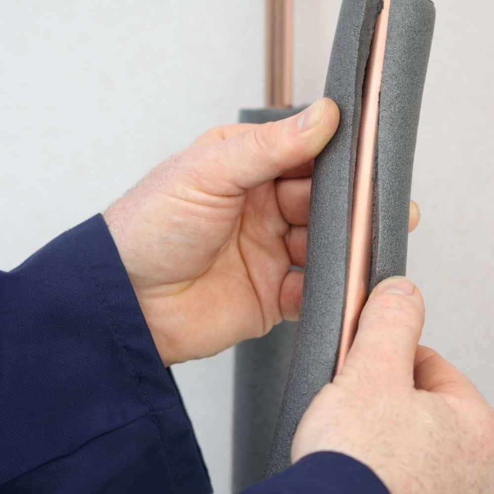 Hände platzieren Isolierschaum um ein Kupferrohr zum Schutz.