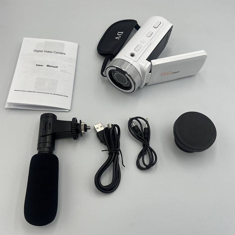 Eine weiße digitale Videokamera mit aufgeklapptem LCD-Bildschirm, ein Mikrofon, USB-Kabel, eine Objektivkappe und eine Bedienungsanleitung werden auf einer grauen Oberfläche angezeigt.