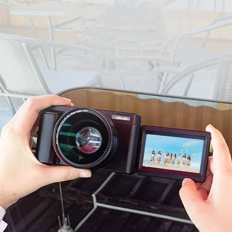 Eine Person hält eine Digitalkamera mit offenenem Bildschirm, auf dem ein Gruppenfoto von neun Personen zu sehen ist, die im Freien unter einem blauen Himmel stehen.