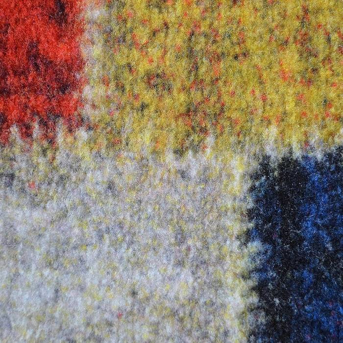 Nahaufnahme eines farbenfrohen, strukturierten Stoffes mit roten, gelben, blauen und grauen Flecken, die ein raues, gewebtes Muster zeigen.