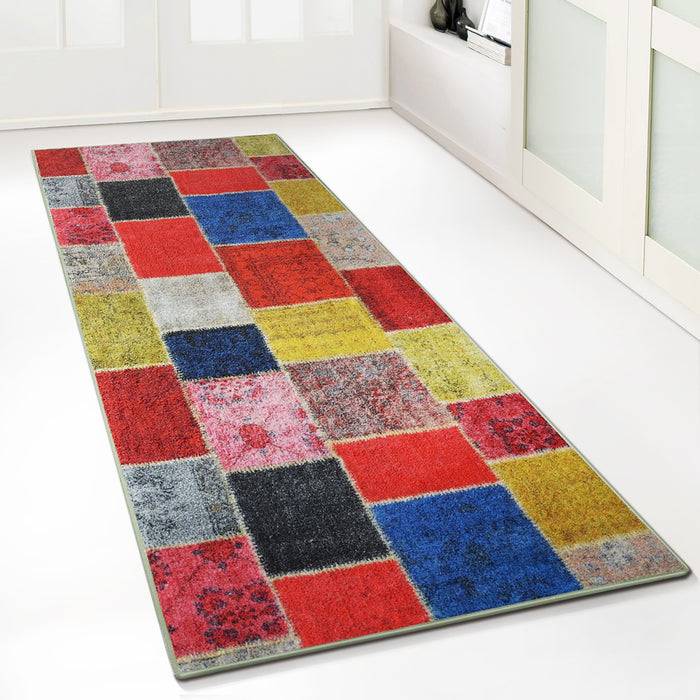 Ein rechteckiger Flurläufer mit einem Patchwork aus roten, blauen, gelben, grauen und rosa Quadraten und Rechtecken, der auf einem hellen Boden platziert ist.