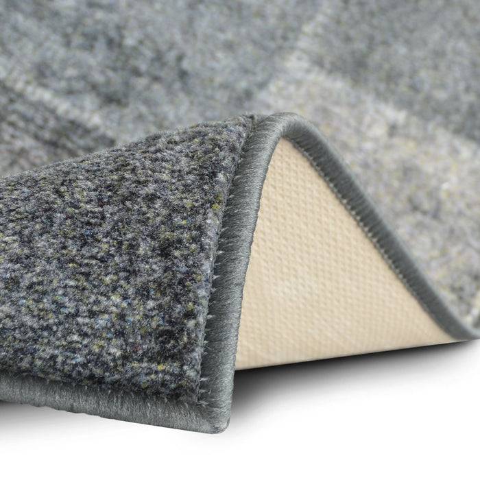 Eine Nahaufnahme der Ecke eines grauen Teppichs, die eine strukturierte Oberfläche und eine hellfarbige Rückseite zeigt und die Materialqualität hervorhebt.