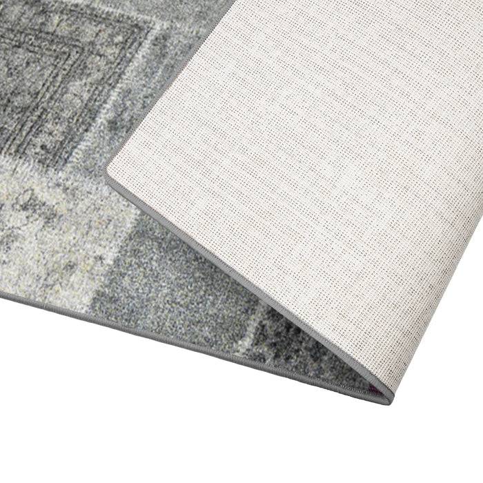 Ein gefalteter Bereichsteppich mit quadratischem Muster in Grautönen, der die strukturierte Rückseite in Beige zeigt.