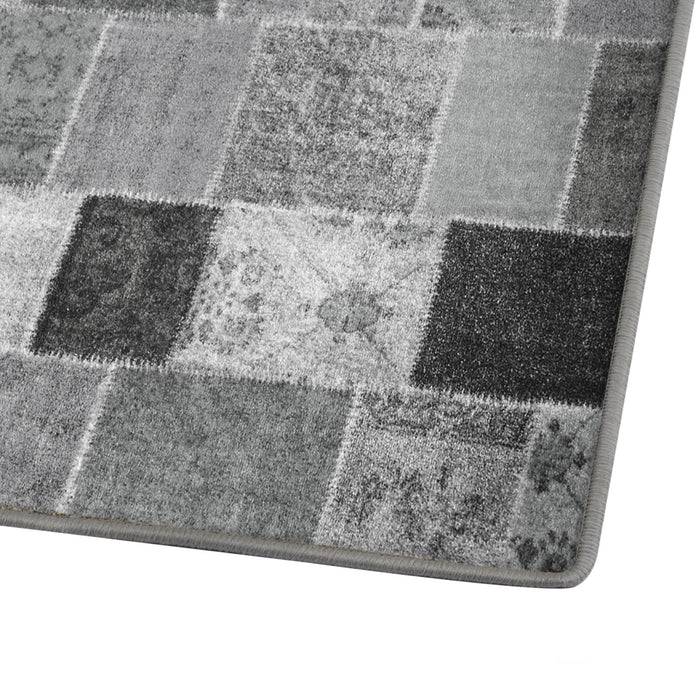 Ein rechteckiger Teppich mit einem Patchwork-Muster in verschiedenen Grautönen, mit floralen und strukturierten Designs in jedem Quadrat.
