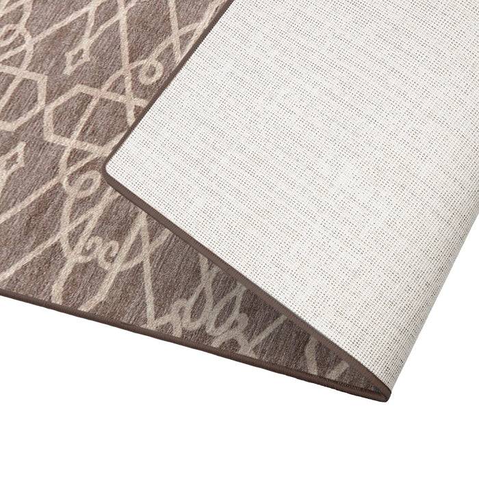 Ein brauner Bereich Teppich mit einem weißen geometrischen Muster, teilweise aufgerollt, um die rutschfeste Rückseite zu zeigen.