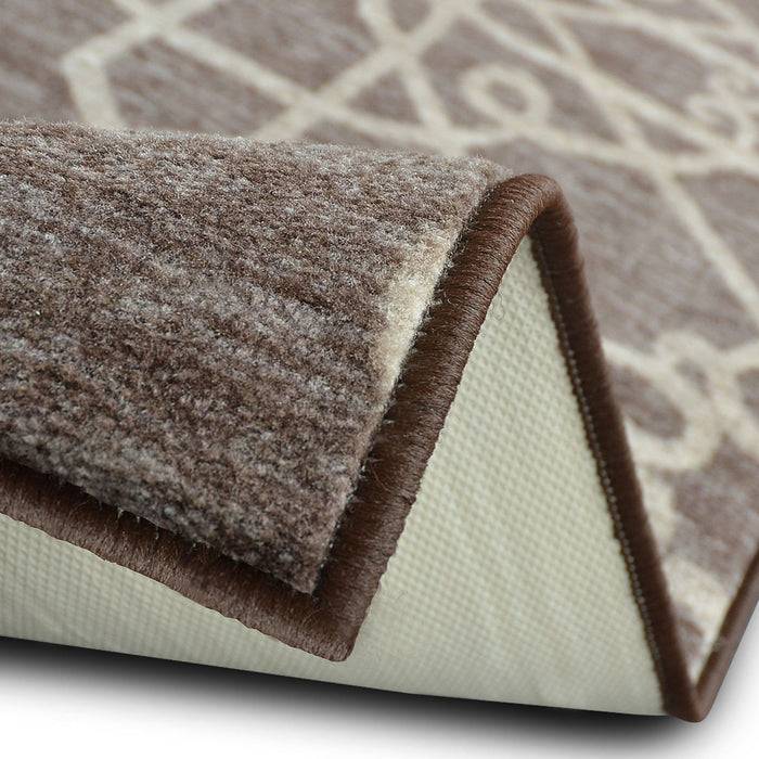 Eine Nahaufnahme eines braunen Teppichs mit einem beigen geometrischen Muster, das seine dicke Textur und eine umgeklappte Ecke zeigt, um die rutschfeste Unterseite zu enthüllen.