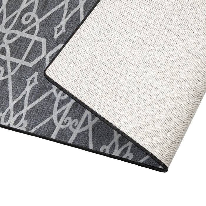 Ein grau-weiß gemusterter Teppich, teilweise aufgerollt, der sein detailliertes geometrisches Design auf einer strukturierten Oberfläche zeigt.