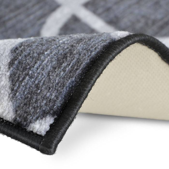 Nahaufnahme einer Ecke eines grau gemusterten Teppichs, die die Textur, die schwarze Kante und die weiße Rückseite zeigt.