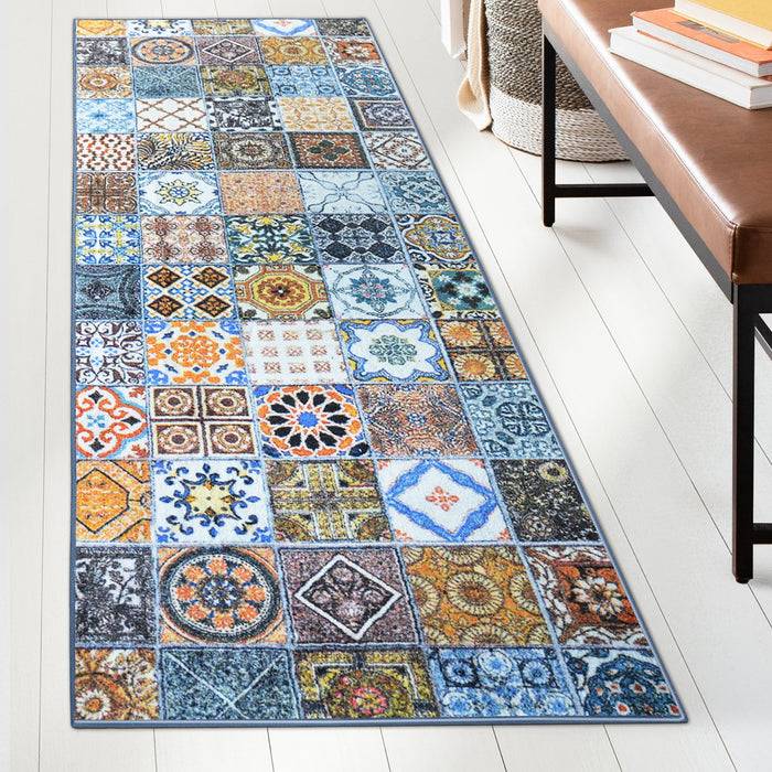 Ein bunter Teppich mit einer Flickendecke aus verschiedenen geometrischen und floralen Mustern liegt auf einem Holzboden neben einem Tisch mit gestapelten Büchern.