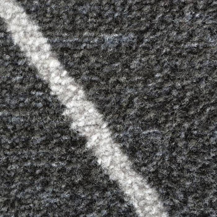 Nahaufnahme eines strukturierten, dunkelgrauen Teppichs mit einer hellgrauen Diagonallinie, die hindurchläuft.