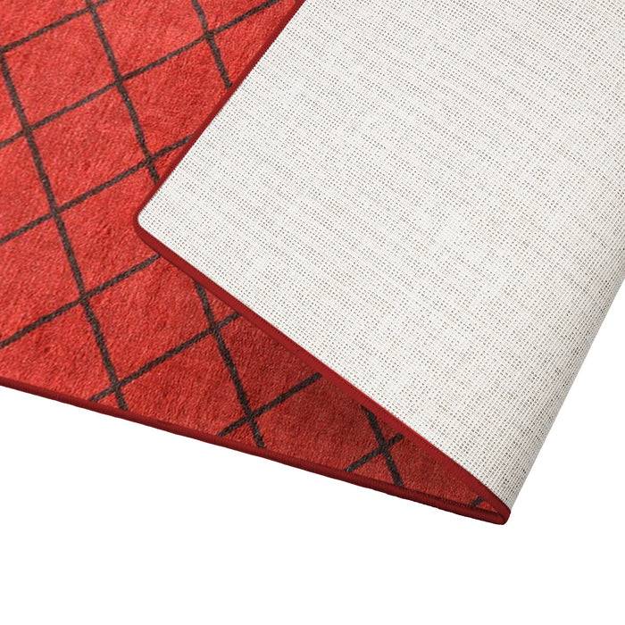Ein roter Bereichsteppich mit schwarzem Kreuzmuster, teilweise gefaltet, um seine weiße Unterseite und Textur zu zeigen.