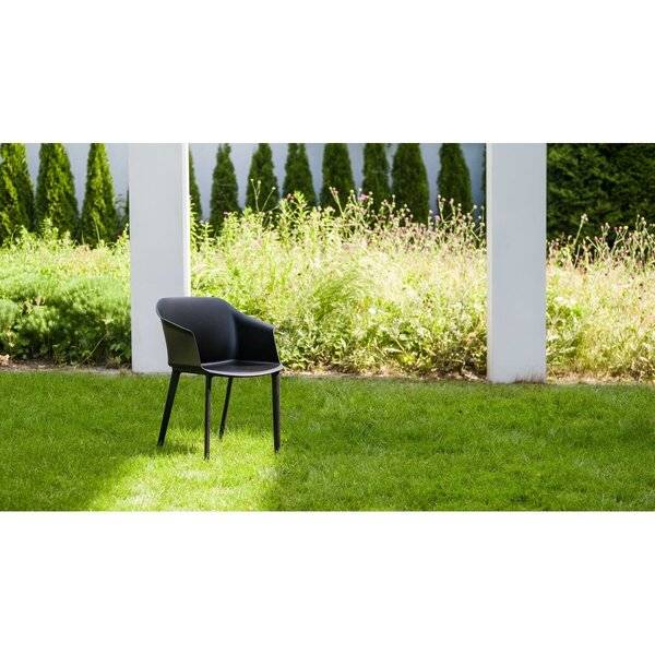 Schwarzer Stuhl auf einem sonnigen grünen Rasen in einem Garten mit weißen Säulen, Büschen und hohen Bäumen im Hintergrund.