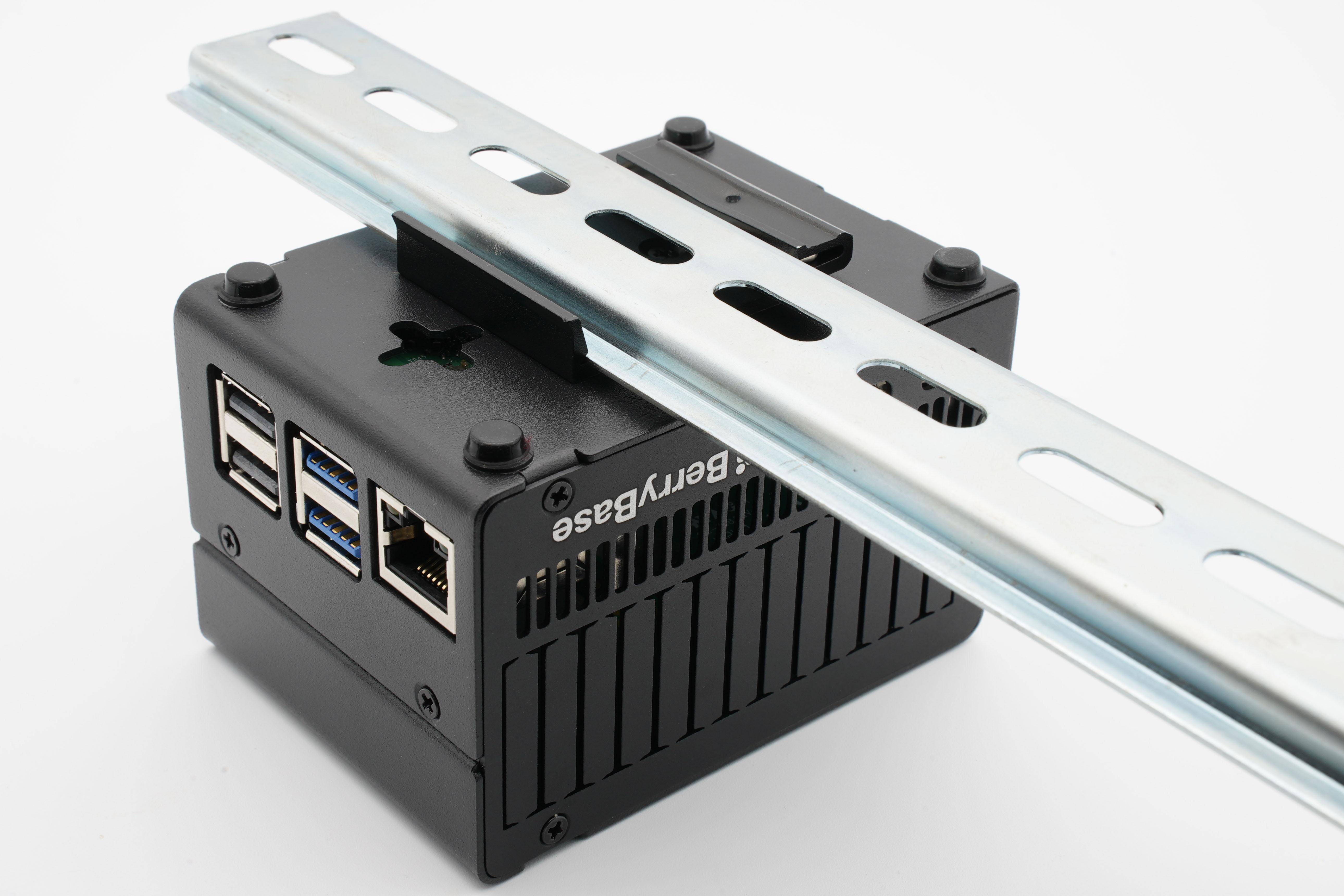 Ein Raspberry-Pi-Gerät in einem schwarzen Metallgehäuse, das auf einer Metallhalterung montiert ist. An der Seite sind mehrere USB- und Ethernet-Anschlüsse sichtbar.