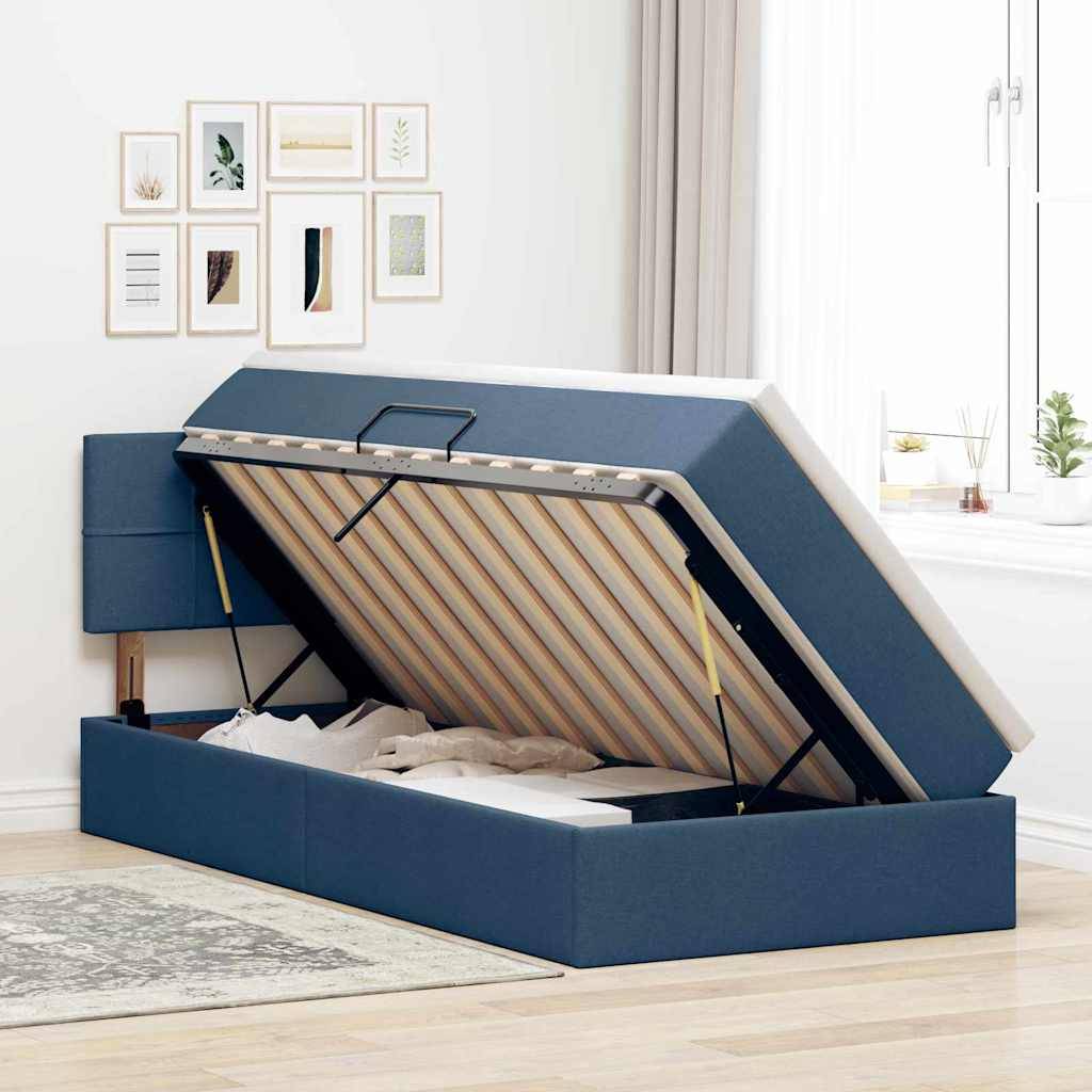Ein blau gepolstertes Bett mit einem offenen hydraulischen Aufbewahrungssystem unter der Matratze in einem hellen Raum mit gerahmten Kunstwerken an der Wand.