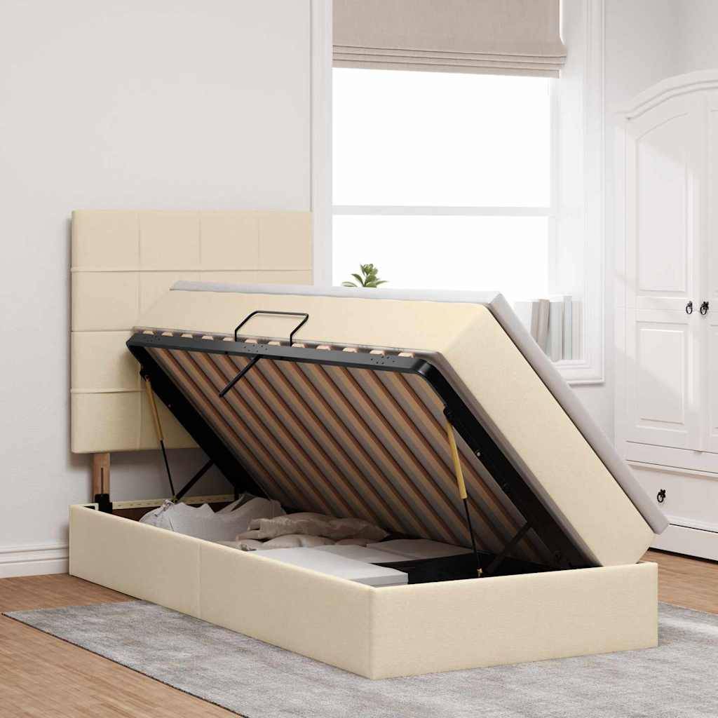 Ein beiges Ottomanenbett mit hochgehobenem Kopfteil, das den Stauraum darunter zeigt, positioniert in einem hellen Raum mit weißen Möbeln.