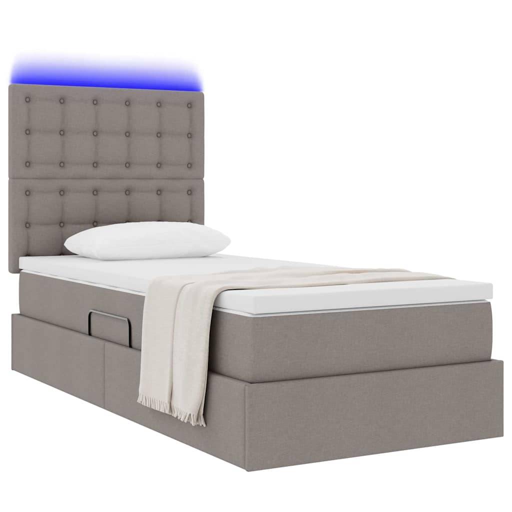 Ein einzelnes Bett mit gepolstertem Kopfende, das mit einem blauen LED-Lichtstreifen ausgestattet ist, ein weißes Kissen und eine hellbeige Decke über dem Fußende drapiert.