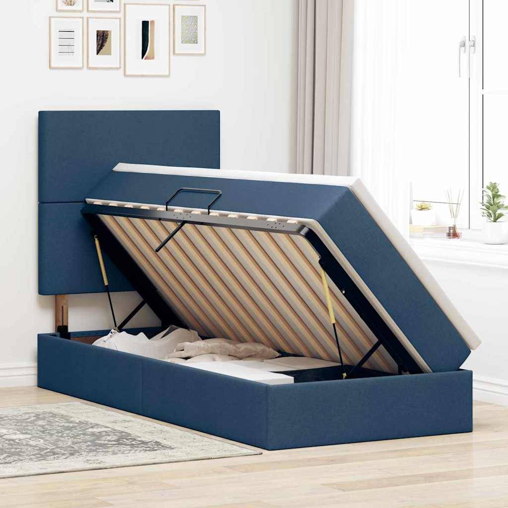 Ein blau gepolstertes Bett mit einem offenen Stauraum unter der Matratze, der Platz zum Lagern freigibtt. In der Nähe befindet sich ein Fenster mit leichten Vorhängen.