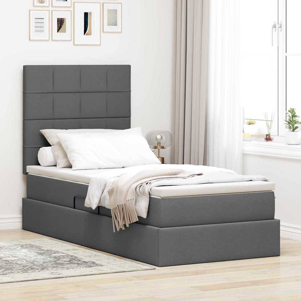Ein modernes Schlafzimmer mit einem grau gepolsterten Bett mit Schubladen zur Aufbewahrung, weißer Bettwäsche, einer karierten Decke und einem gepolsterten Kopfteil neben einem Fenster.