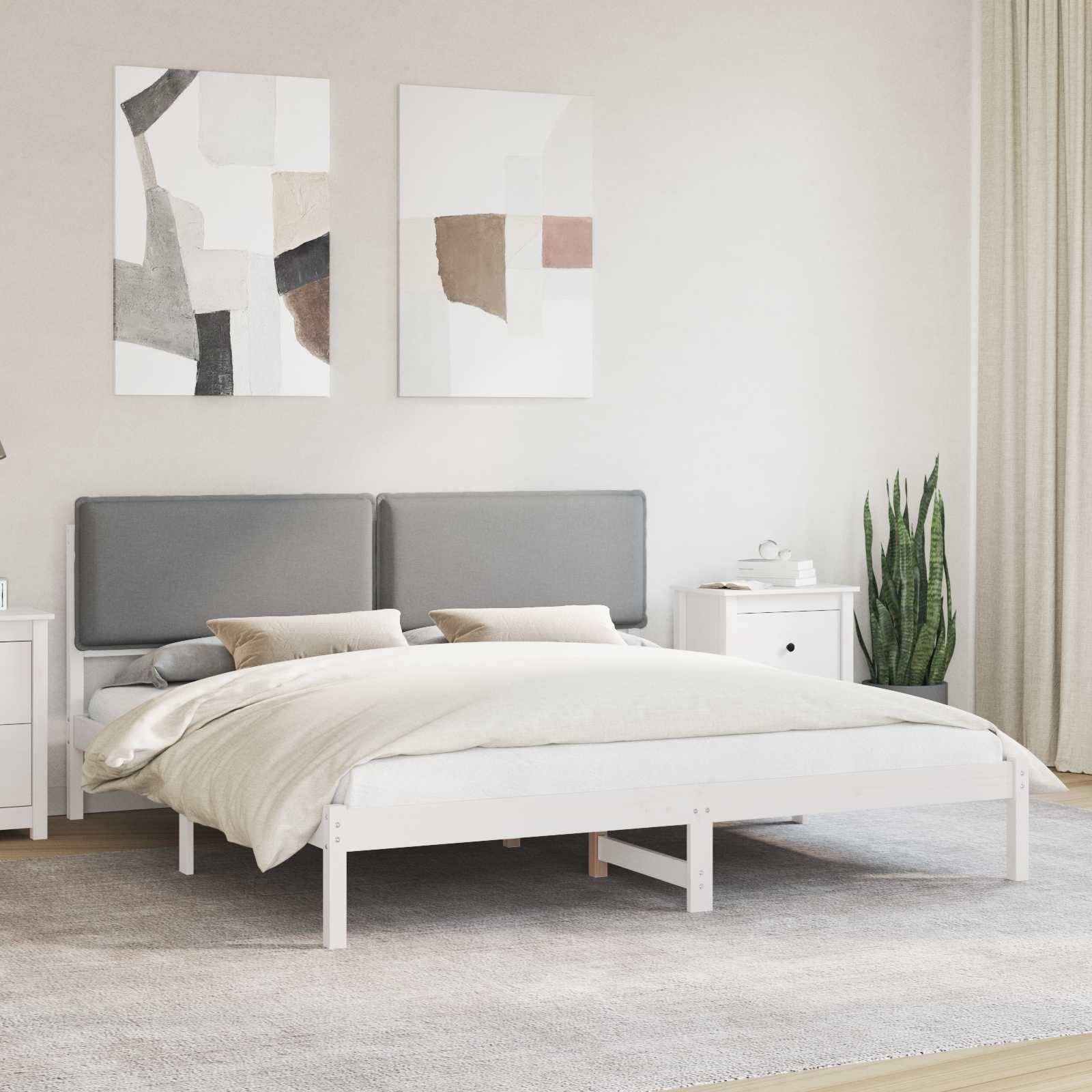 Ein modernes Schlafzimmer mit einem weißen Bett, grauem Kopfteil und abstrakter Wandkunst. Auf jeder Seite des Bettes befinden sich Nachttische und Pflanzen.