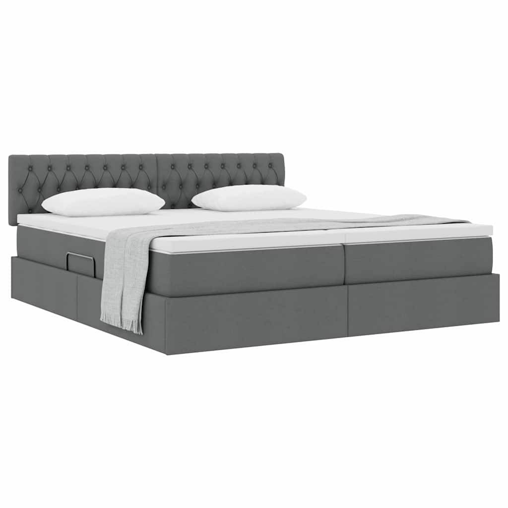 Ein grau gepolstertes Bett mit gestepptem Kopfteil, zwei weißen Kissen, einer Matratze und einer zusammengefalteten hellgrauen Decke.