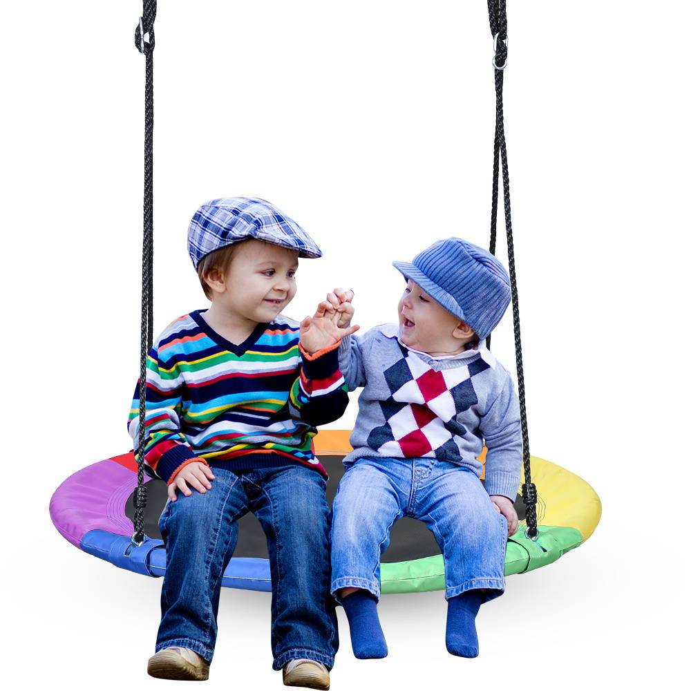 Zwei kleine Kinder, die bunte Hüte und Pullover tragen, halten sich freudig an den Händen, während sie auf einer regenbogenfarbigen Schaukel vor weißem Hintergrund sitzen.