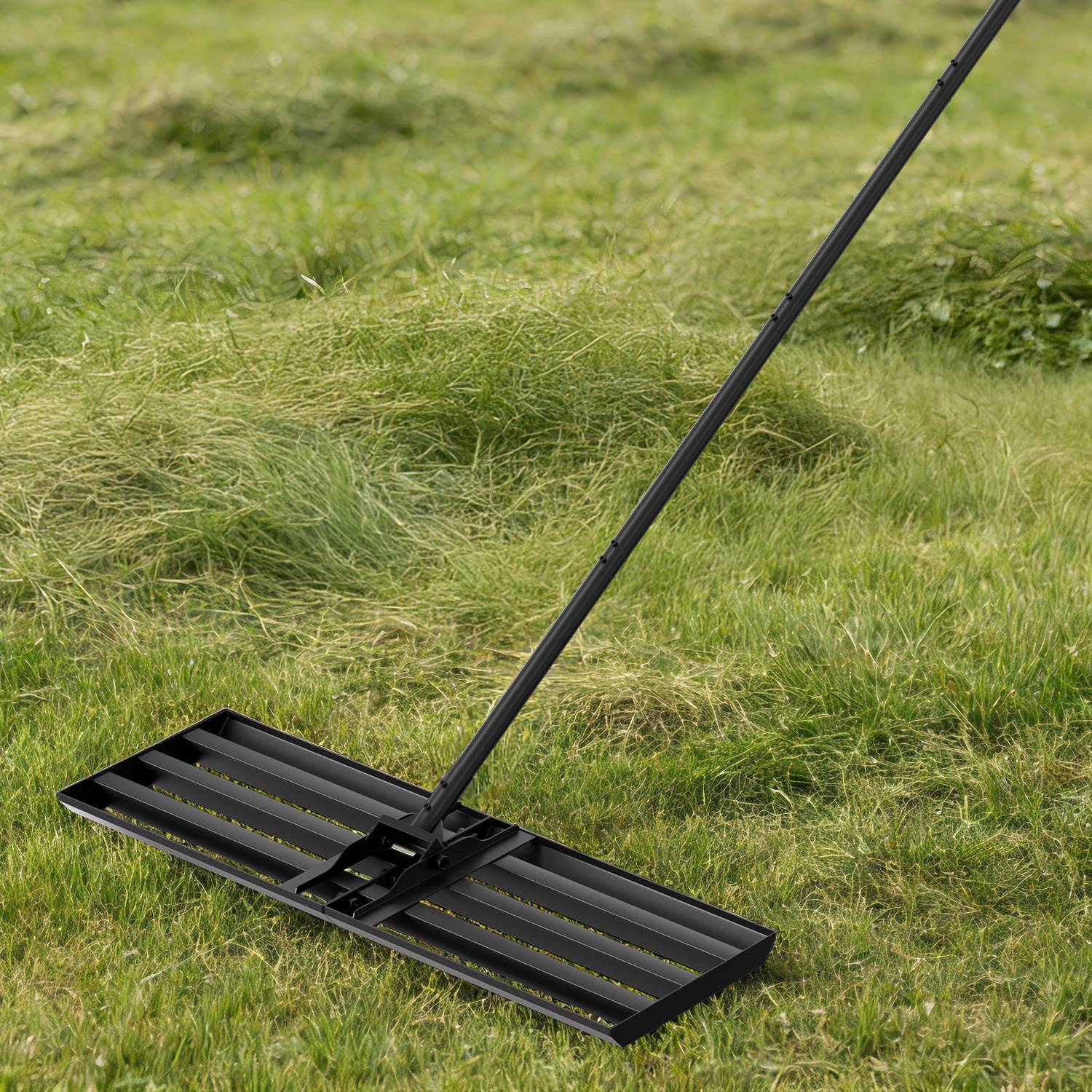 Ein schwarzer Rasennivellierrechen auf grünem Gras mit unebenen Stellen.