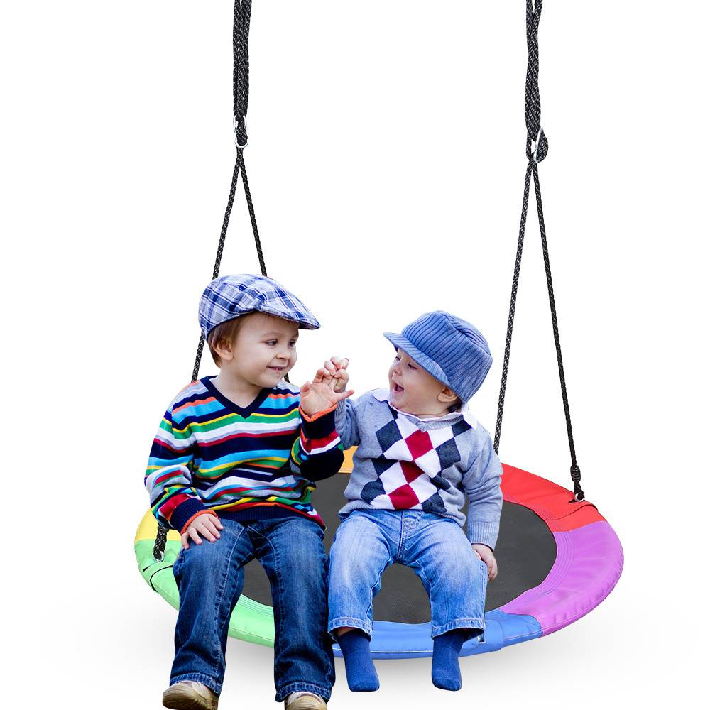Zwei kleine Kinder sitzen auf einer farbenfrohen runden Schaukel. Das Kind auf der linken Seite trägt einen gestreiften Pullover und eine Schiebermütze, das Kind auf der rechten Seite trägt einen Pullover mit Rautenmuster und eine Schiebermütze. Beide lächeln.