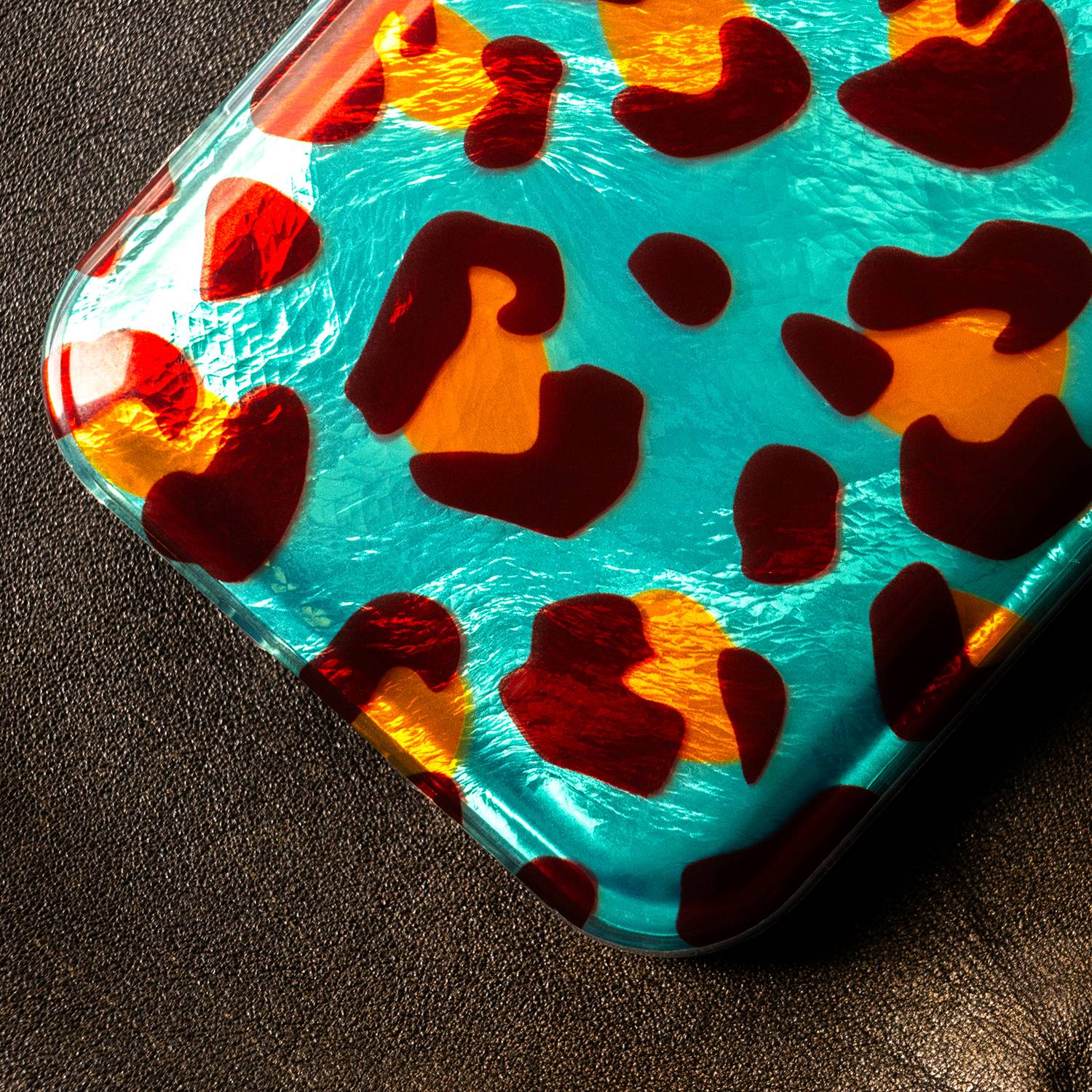 Eine Kunststoffbeutel mit glänzender Oberfläche und abstrakten rot-orangefarbenen Mustern auf einem Blaugrün-Hintergrund liegt auf einer strukturierten, dunklen Oberfläche.