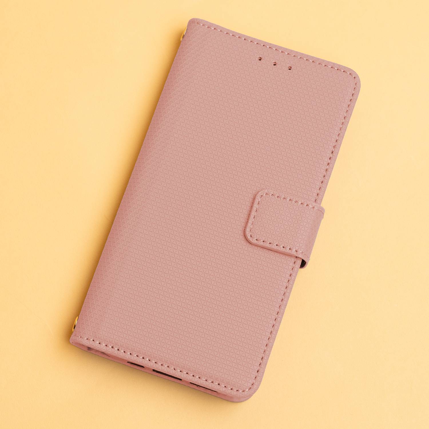 Ein geschlossenes rosa Smartphone-Etui mit strukturierter Oberfläche und magnetischer Verschluss, vor einem einfachen gelben Hintergrund.