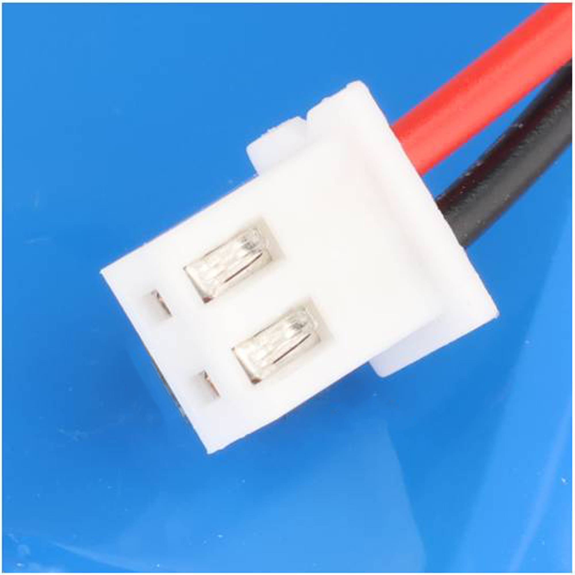 Nahaufnahme eines weißen zweipoligen Elektrosteckers mit roten und schwarzen Kabeln auf blauem Hintergrund.