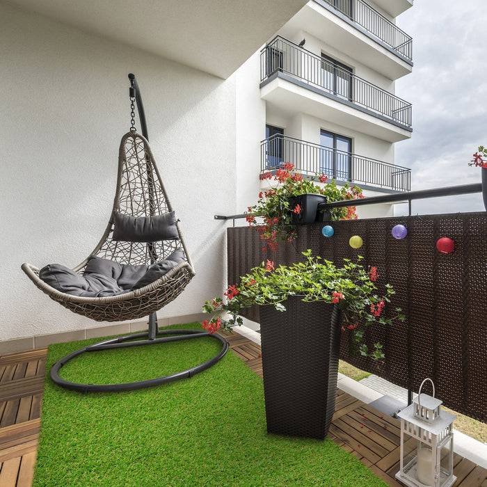 Moderner Balkon mit hängendem Stuhl, grünem Kunstrasen, Topfpflanzen und dekorativen Laternen vor urbaner Gebäudekulisse.