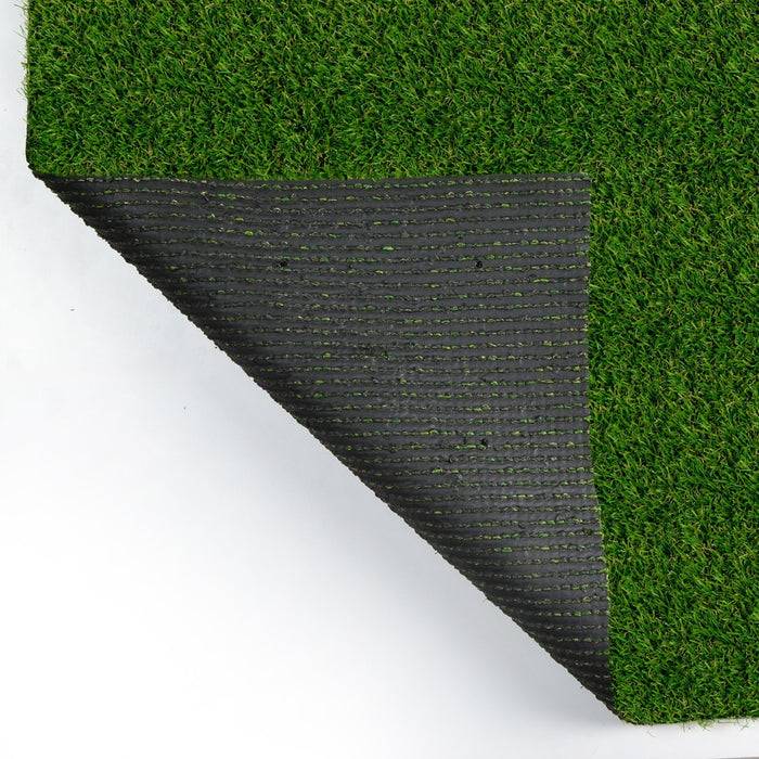 Eine umgeknickte Ecke einer rechteckigen Kunstrasenumrandung zeigt ihre schwarze Gummirückseite. Die Grasfasern sind dicht und lebhaft grün.